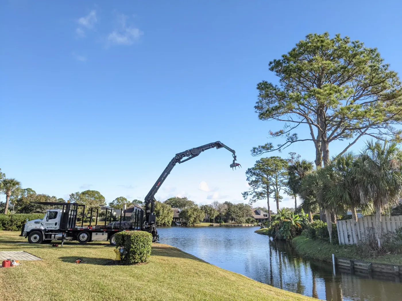 Branded crane truck with grapple on a lakefront lawn — crane tree removal in Jacksonville, FL by Jax Tree Removal