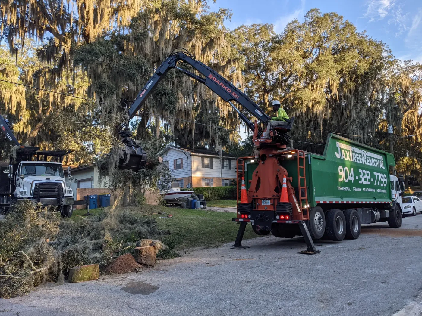 Branded crane truck lifting brush with the grapple under mossy oaks — crane tree removal in Jacksonville, FL by Jax Tree Removal