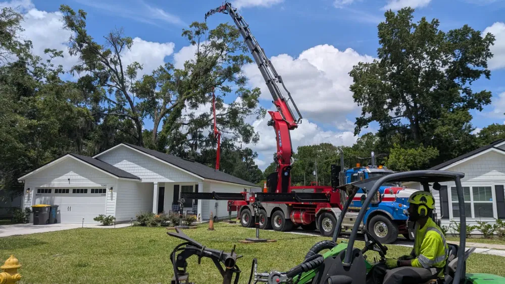 Jax Tree Removal red Effer knuckle-boom crane on a blue Western Star truck reaching over a white home, a red spider lift behind it and a green mini loader in front, Jacksonville, FL