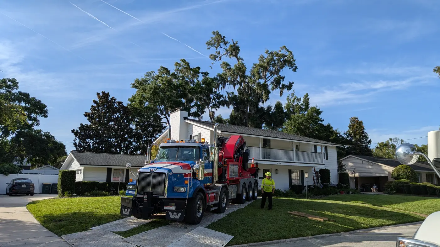 Jax Tree Removal blue Western Star truck with a red Effer knuckle-boom crane staged on the driveway of a two-story white home before a tree removal in Jacksonville, FL