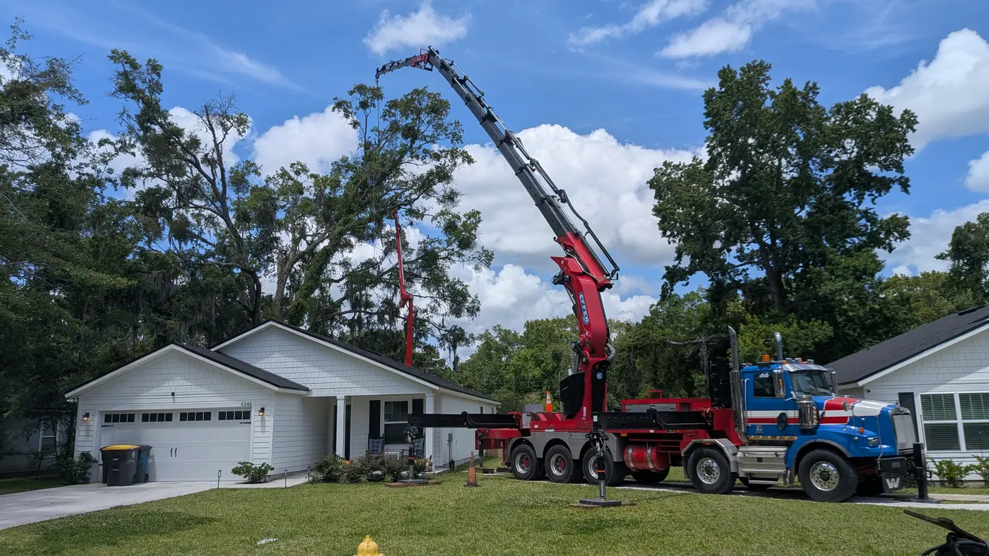 Jax Tree Removal blue Western Star truck with a red knuckle-boom crane reaching over a white home while a red aerial lift works the canopy, Jacksonville, FL