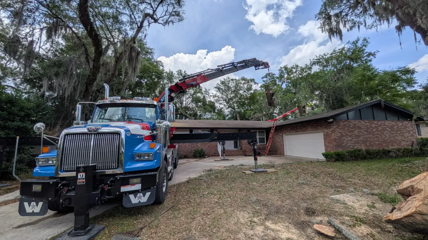 Jax Tree Removal crane truck with boom extended over a brick ranch home for tree work in Jacksonville, FL