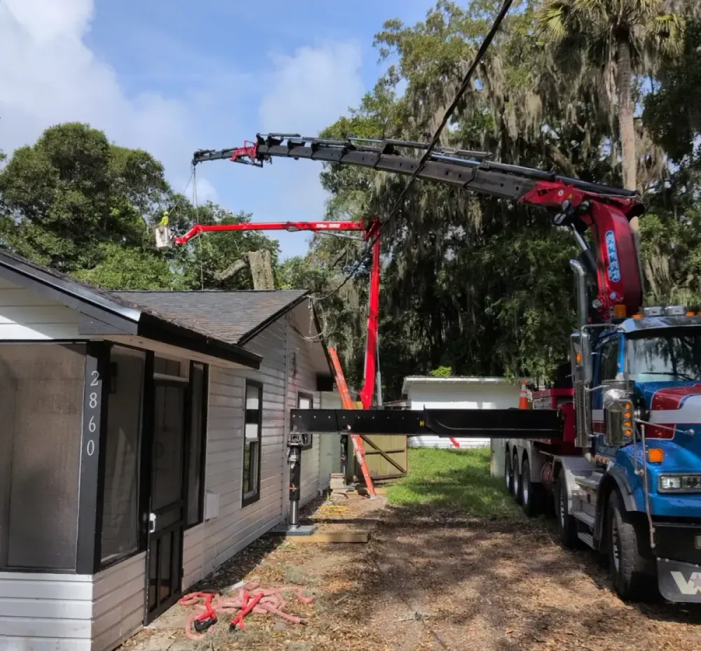 Jax Tree Removal blue crane truck and aerial lift working a moss-draped oak alongside a single-story home in Jacksonville, FL