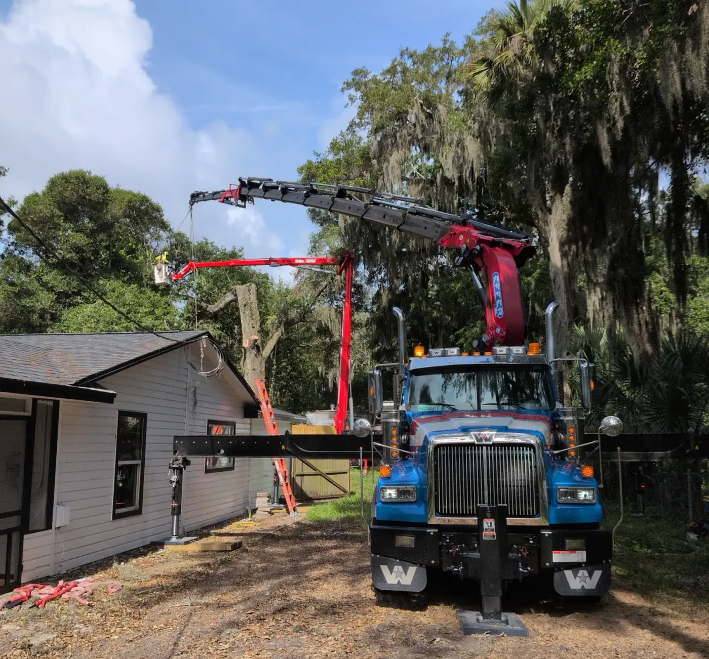 Front view of a Jax Tree Removal crane truck with boom and aerial lift extended over a home for a moss-draped oak removal in Jacksonville, FL
