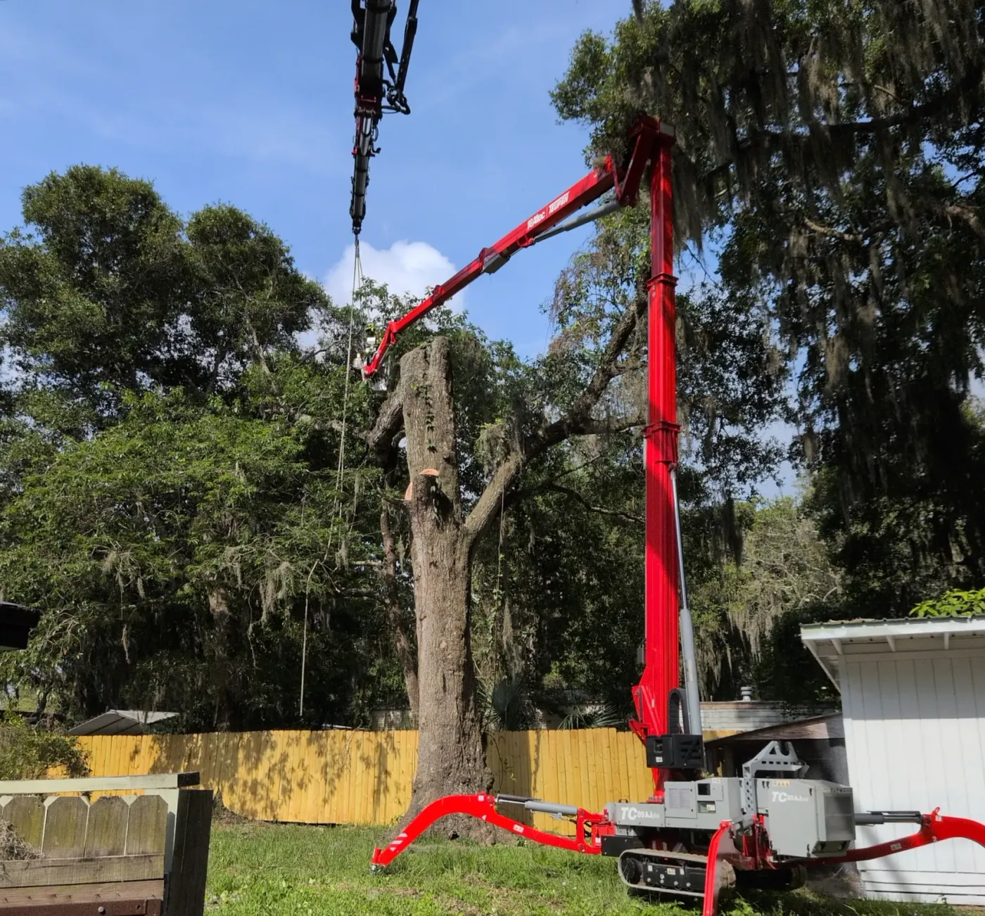 Tracked spider crane with boom extended to a topped backyard oak as a worker rigs the trunk in Jacksonville, FL