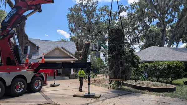 Jax Tree Removal red Effer crane lifting a moss-draped oak trunk section over a brick craftsman home in Mandarin while a groundman directs, Jacksonville FL
