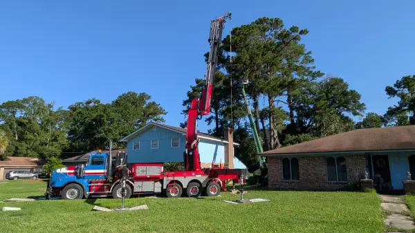 Jax Tree Removal blue-and-red Western Star truck with a red Effer crane boom raised while a green aerial lift reaches into tall pines behind a home in Jacksonville, FL