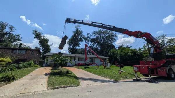 Jax Tree Removal red Effer knuckle-boom crane lifting a strapped oak trunk section while a climber works from a red spider lift on the lawn of a Jacksonville, FL home