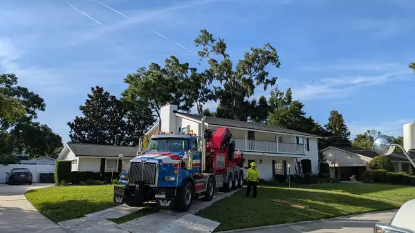 Jax Tree Removal blue Western Star truck with a red Effer knuckle-boom crane staged on the driveway of a two-story white home before a tree removal in Jacksonville, FL