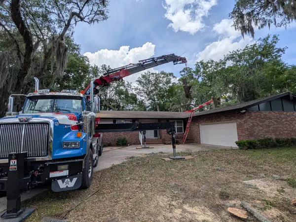 Jax Tree Removal crane truck with boom extended over a brick ranch home for tree work in Jacksonville, FL
