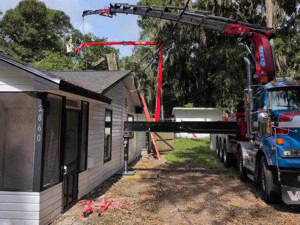 Jax Tree Removal blue crane truck and aerial lift working a moss-draped oak alongside a single-story home in Jacksonville, FL