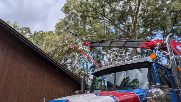 Jax Tree Removal red, white and blue Western Star crane truck with the red Effer knuckle-boom extended while a climber cuts from a red lift beyond a home in Jacksonville, FL