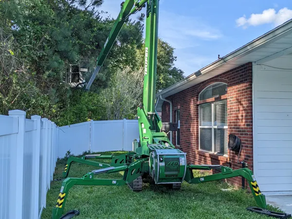 Green spider lift working a tight backyard between a house and fence — tree service in Jacksonville, FL by Jax Tree Removal