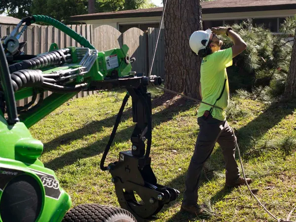 Jax Tree Removal ground worker rigging a line beside a green mini loader — tree service in Jacksonville, FL