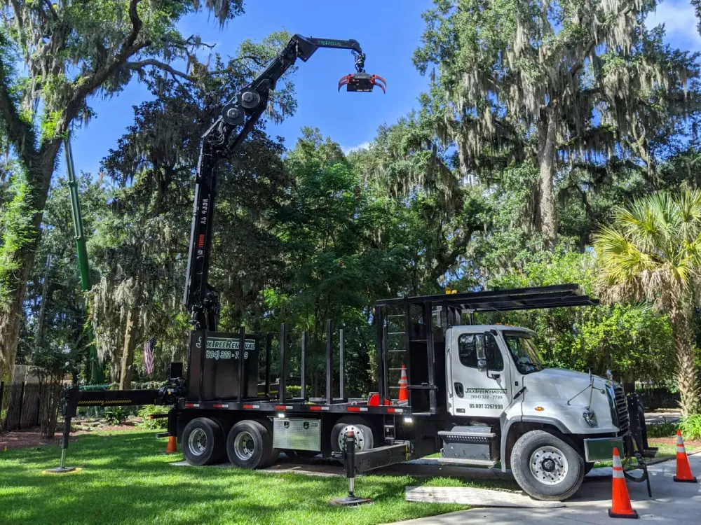Jax Tree Removal knuckle-boom crane truck lifting a large oak trunk section during a commercial removal in Jacksonville, FL