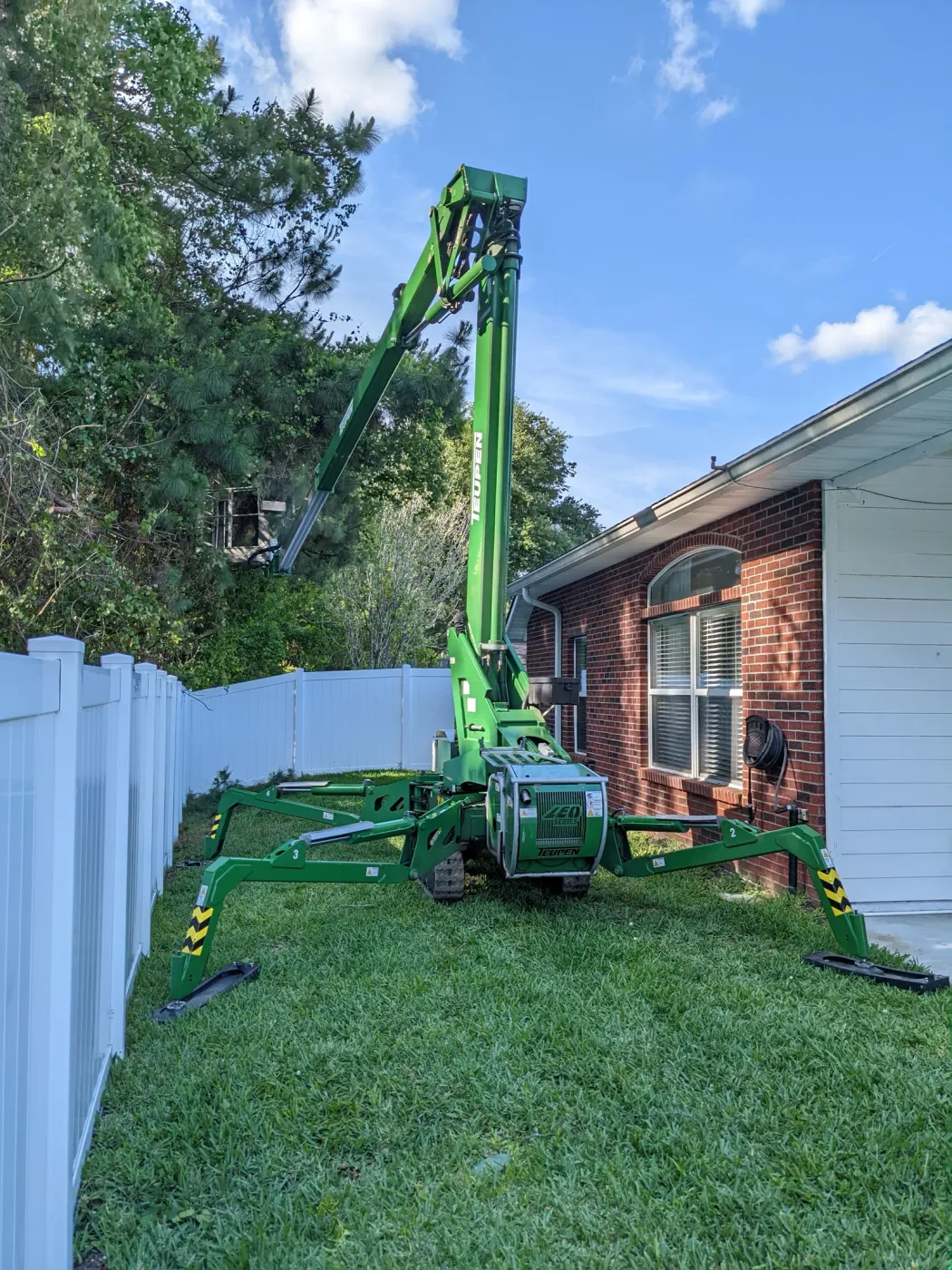 Green spider lift working a tight backyard between a house and fence — tree service in Jacksonville, FL by Jax Tree Removal